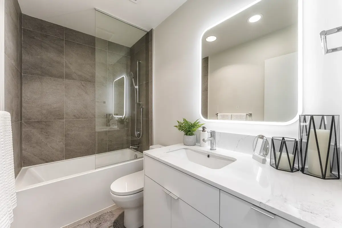 Bathroom with a glass panelled tub and shower in dark tile, candles on the counter