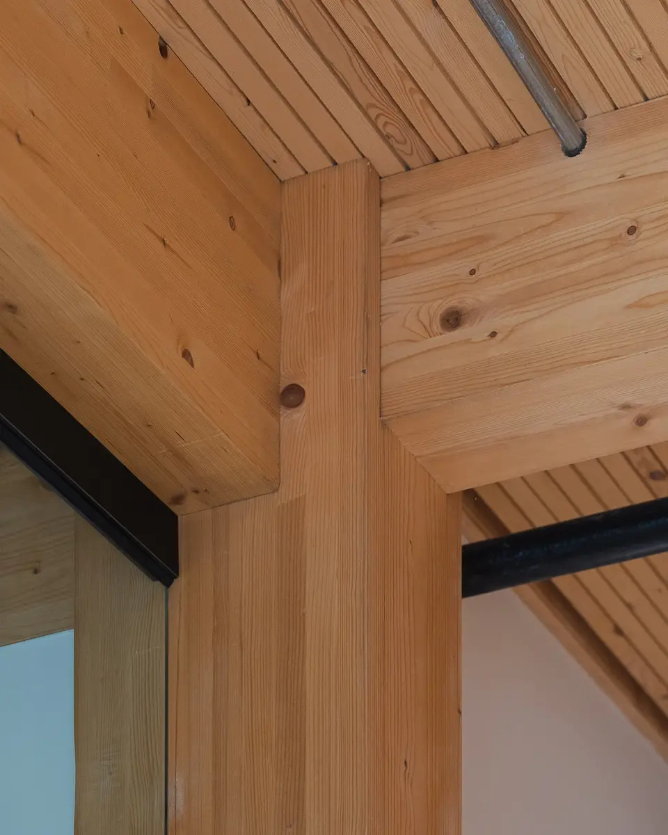 Close on the joint where a timber beam meets a column below the plank ceiling