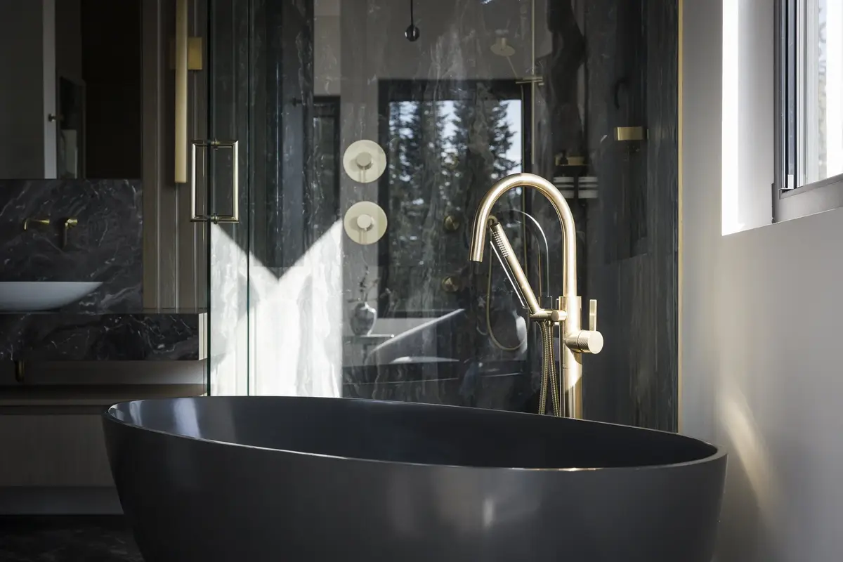 Dark tub and a glass shower in a bathroom lined with dark stone