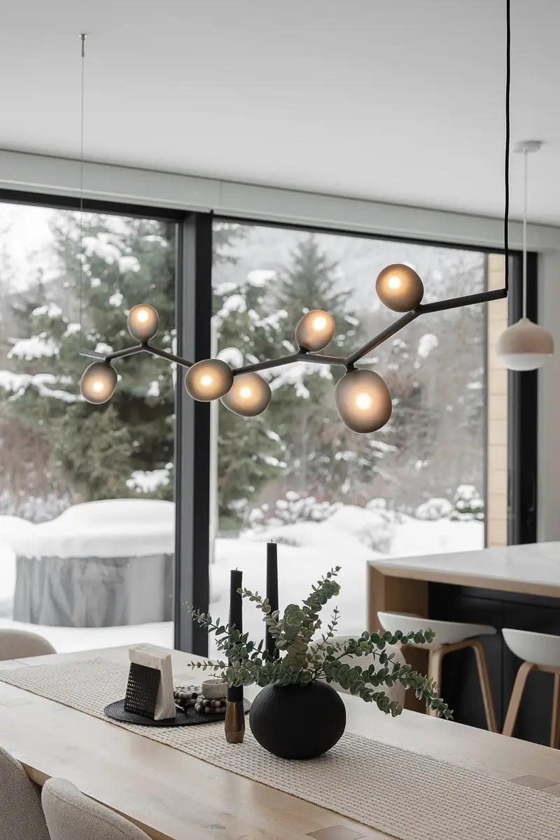 Amber globes on a branching pendant above the dining table, snowy trees at the window