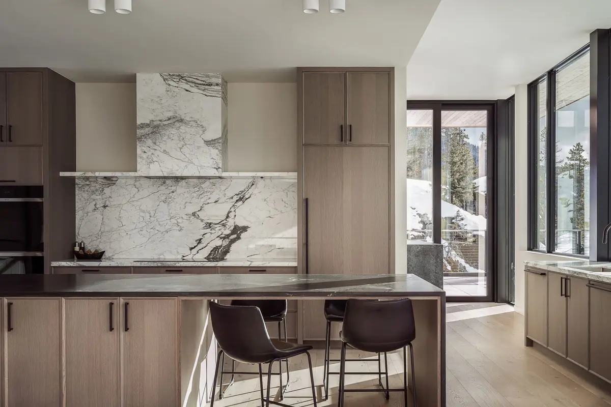 Kitchen with a veined stone backsplash, pale timber cabinetry and a dark stone island