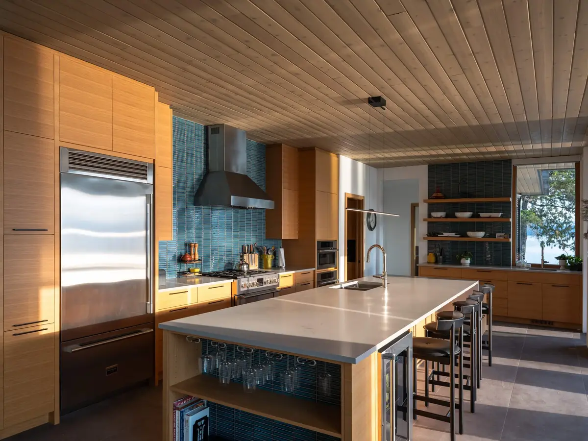 Kitchen with a long island, pale wood cabinetry and a teal tile backsplash