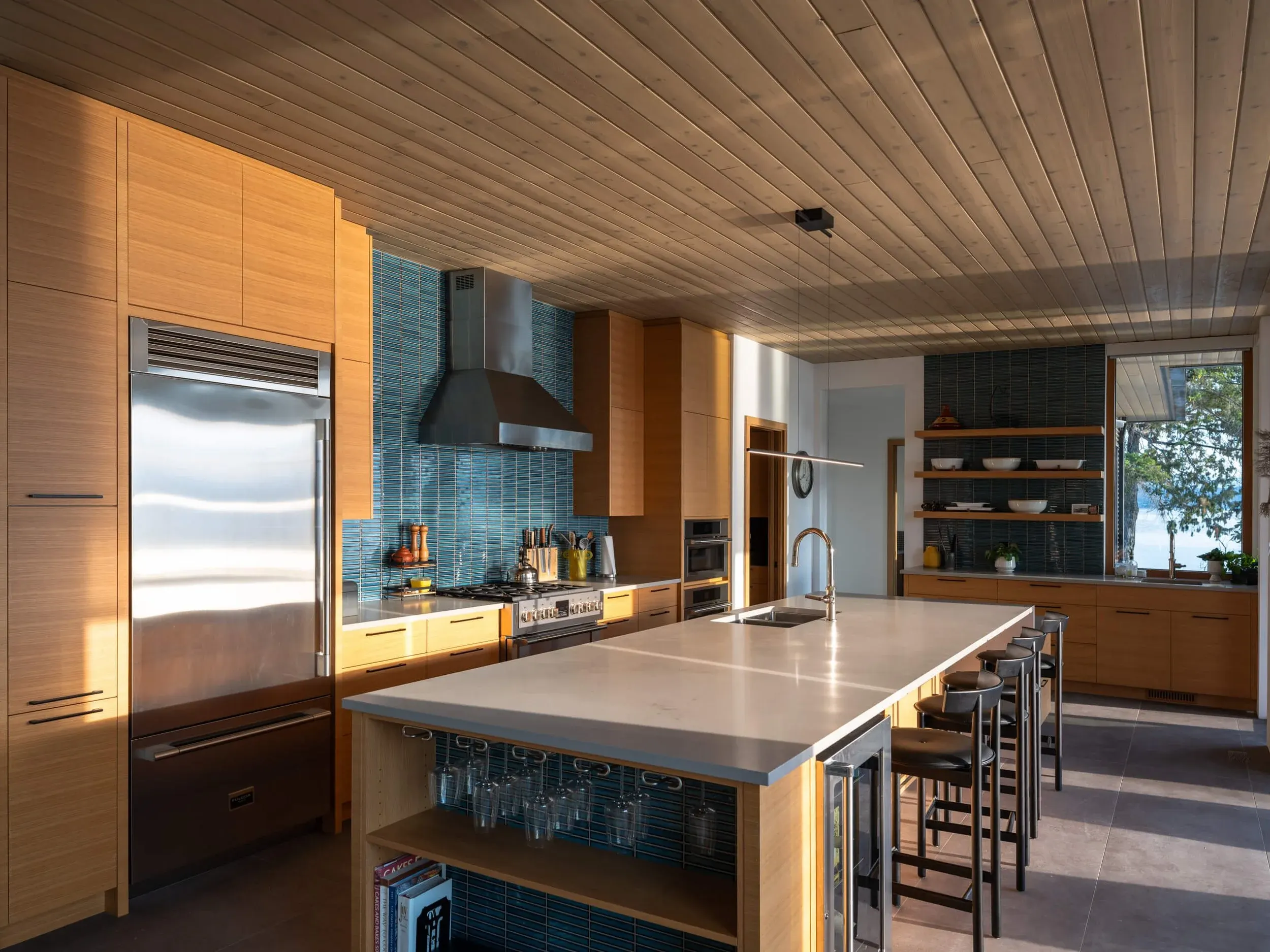 Kitchen with a long island, pale wood cabinetry and a teal tile backsplash
