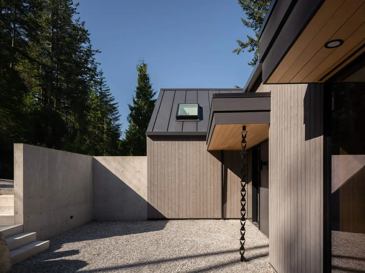 Entry court walled in concrete, a dark rain chain hanging from a pale wood soffit