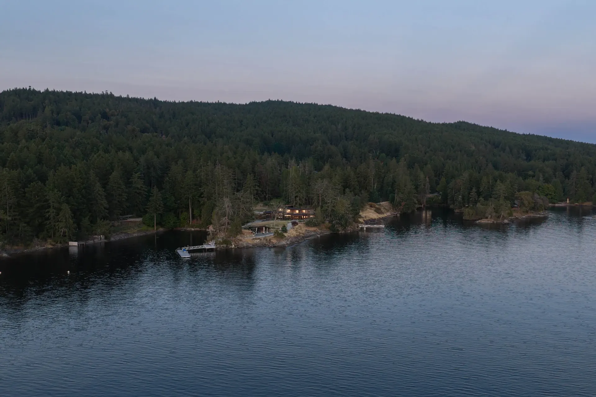 Aerial at dusk, the house set low in the trees along the far shore