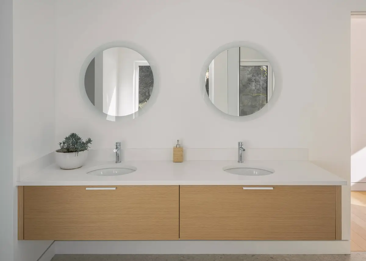 Two round mirrors above a pale wood vanity with twin basins