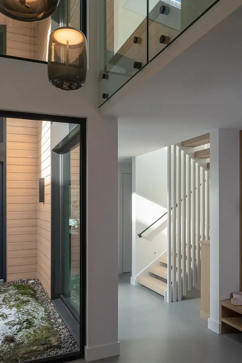 Double height hall beside a glazed light court, a pendant above and the stair beyond