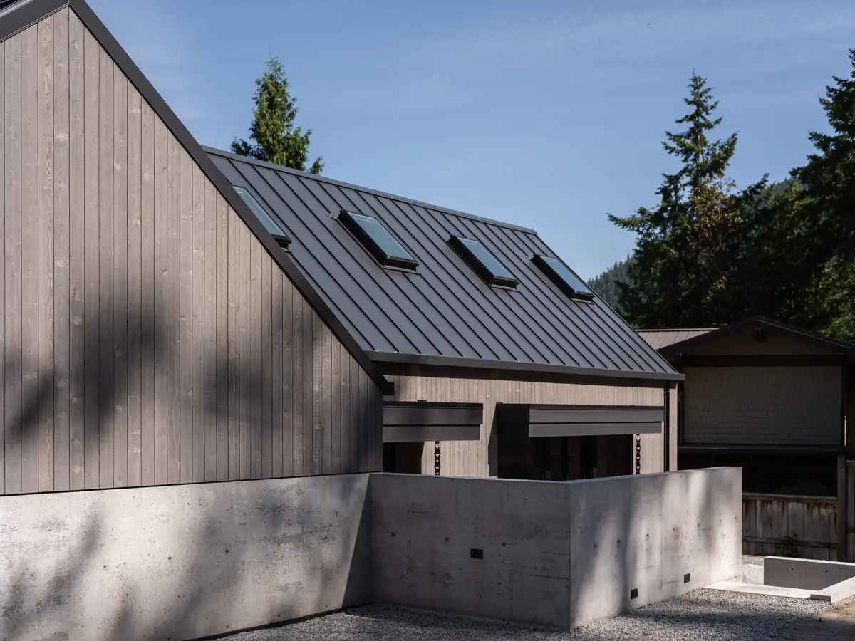 Gable end and a low dark roof with skylights above a concrete retaining wall