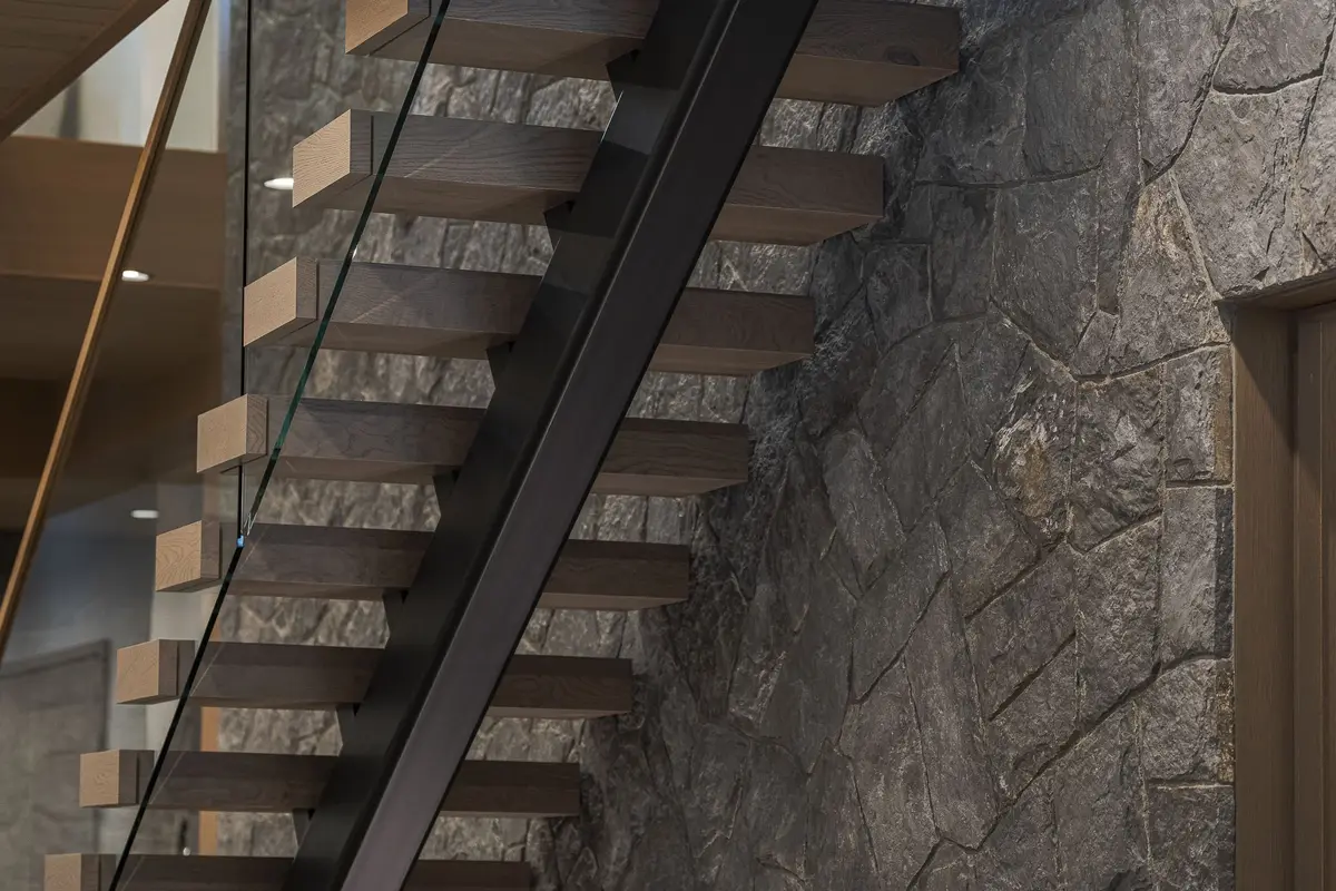 Open stair treads on a black stringer against a wall of rough stone