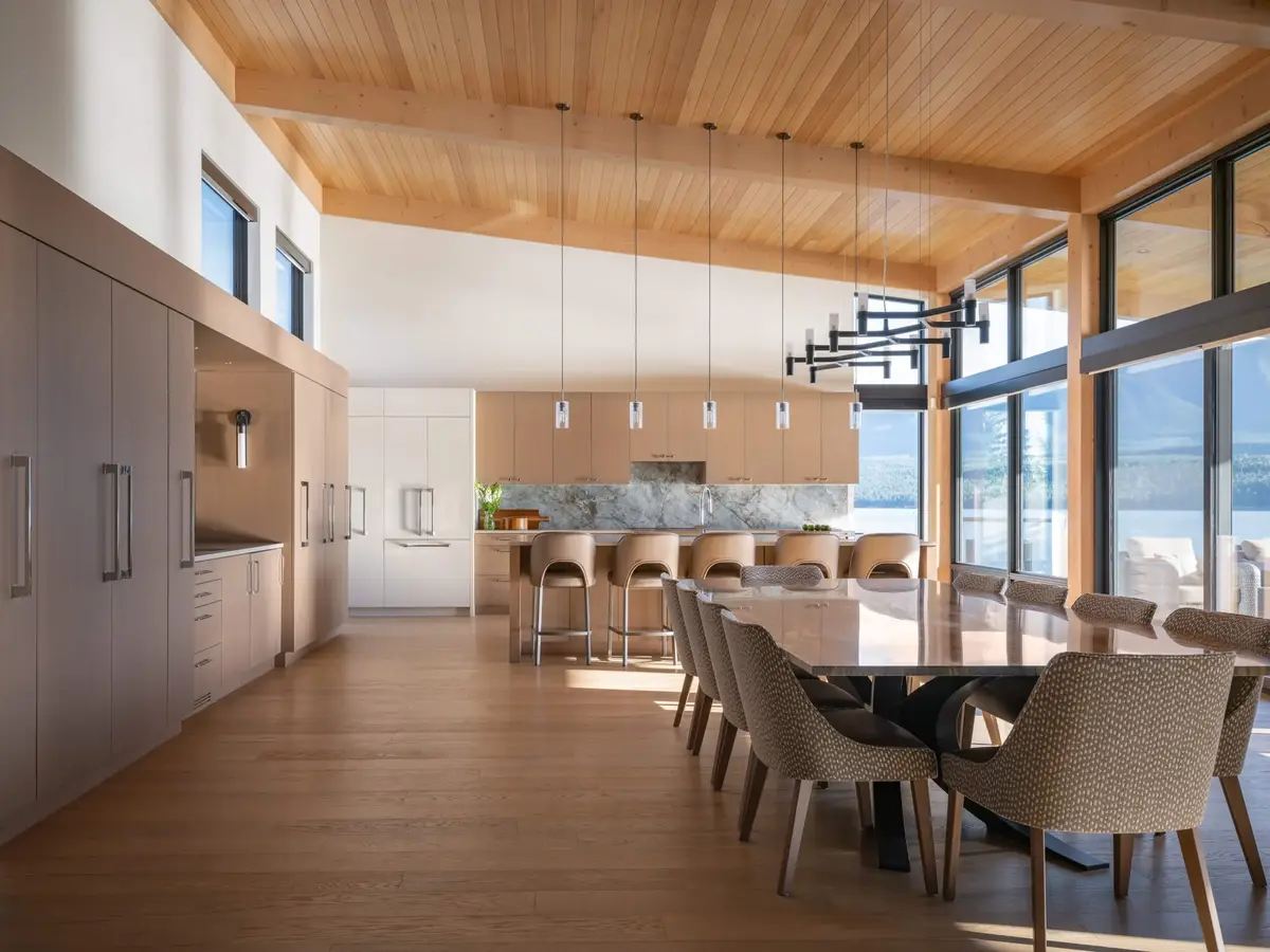 Long room of tall cabinetry, island stools and a dining table running toward the water