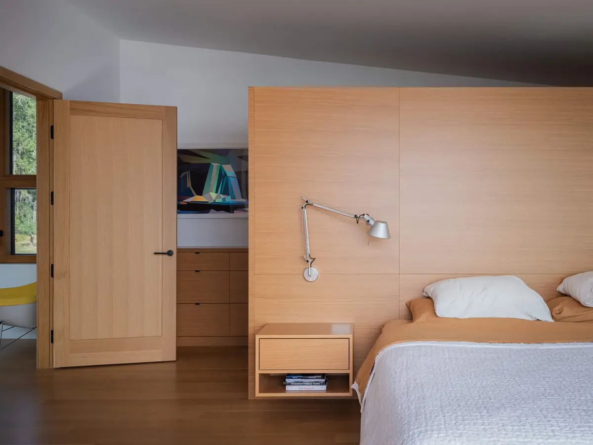 Bedroom with a pale timber headboard wall, a reading lamp and a low nightstand