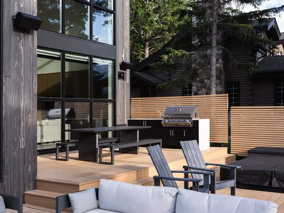 Deck with an outdoor grill and counter, a dining table and chairs beside full height glazing