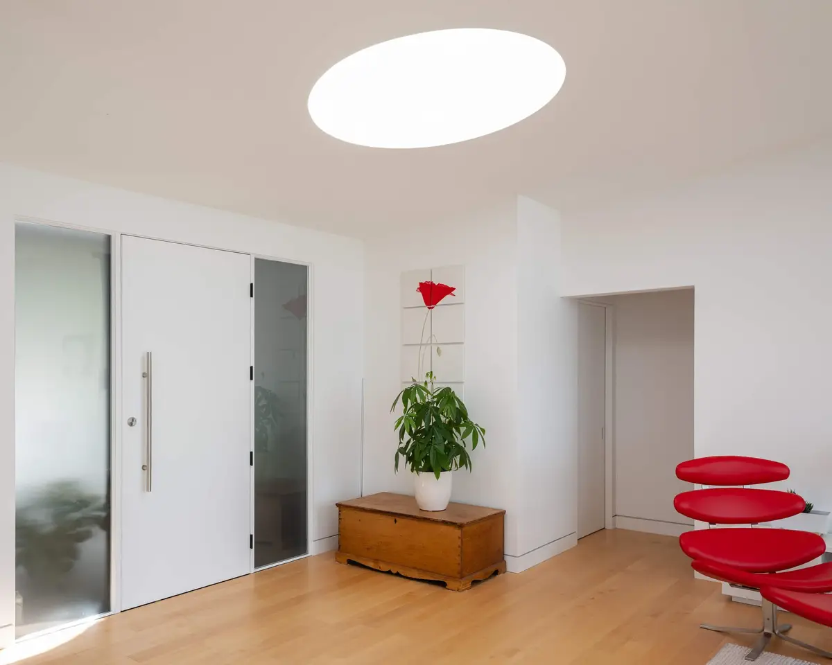 A red moulded lounge chair in the entry hall, oval skylight overhead