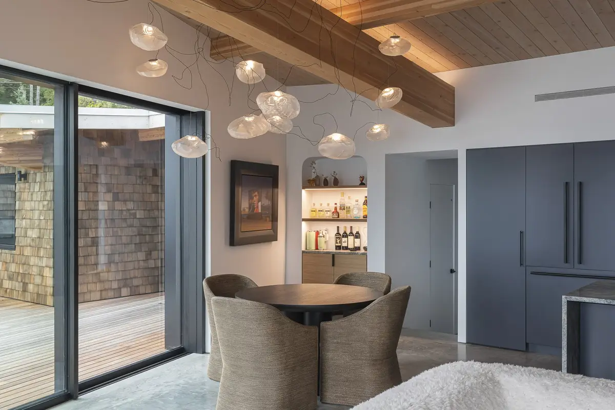 Dining table and chairs below glass pendants, dark cabinets and a bar niche beyond