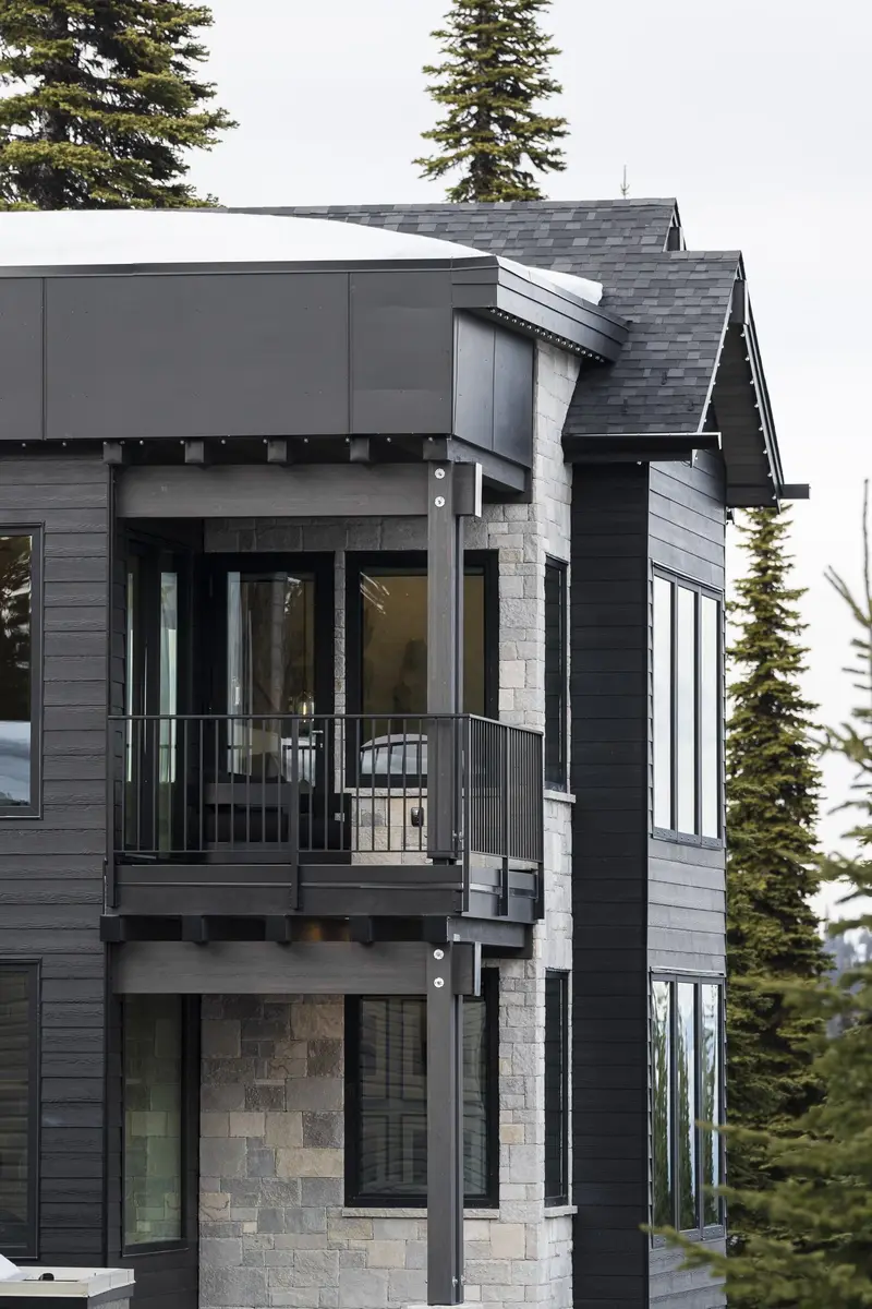 Corner of the house, stone base under dark siding with a covered balcony above