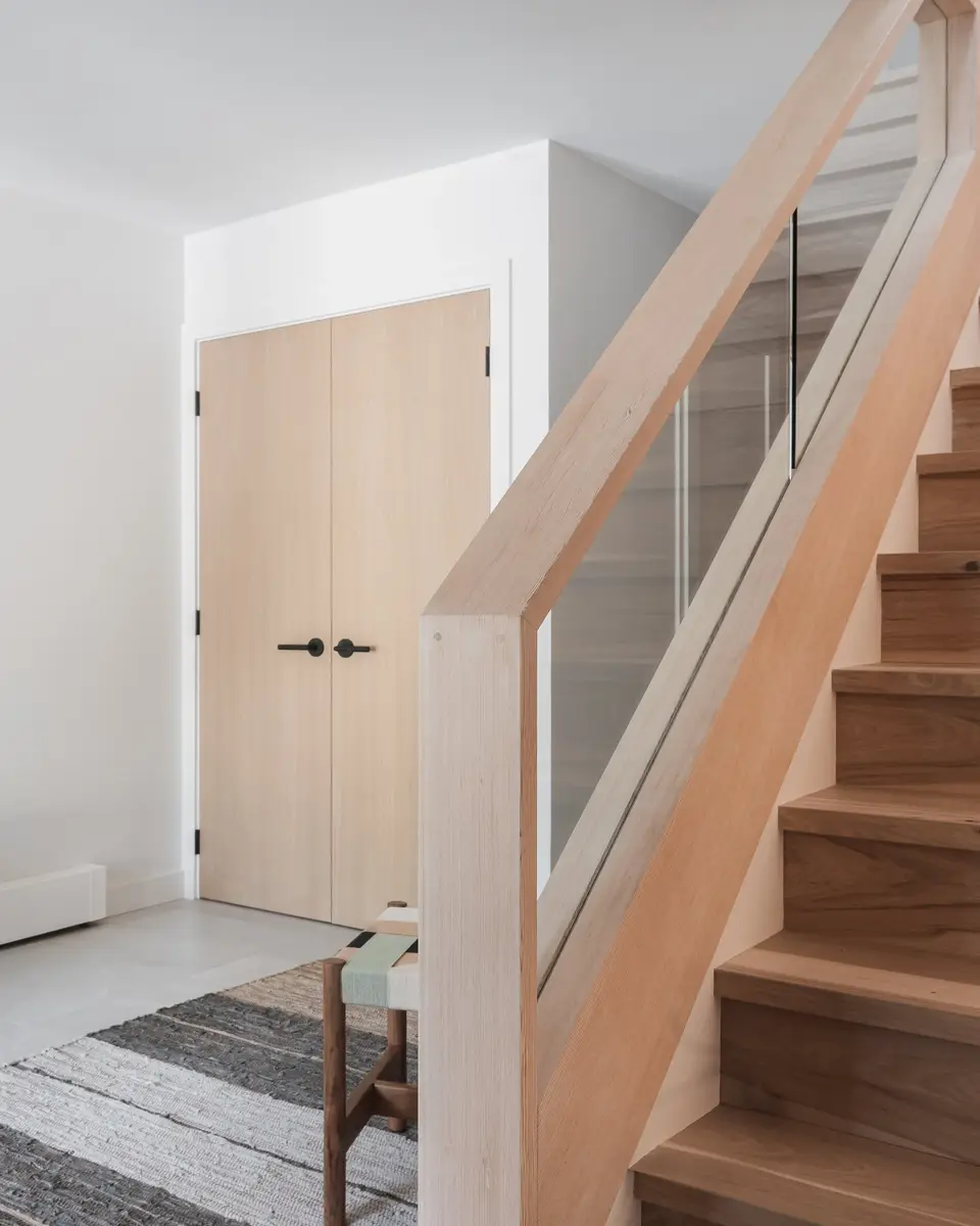 Stair with wood treads behind a glass balustrade, a pale door on the landing