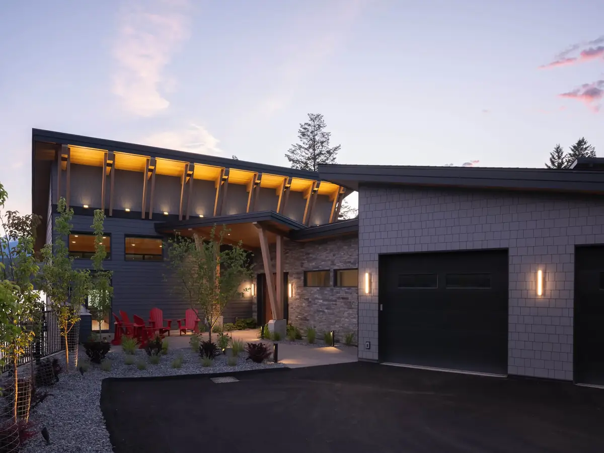 Entry at twilight, roof brackets uplit above red chairs and a dark garage door