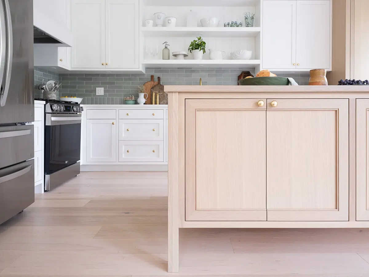 Island end in pale wood seen past the refrigerator, kitchen and open shelves beyond