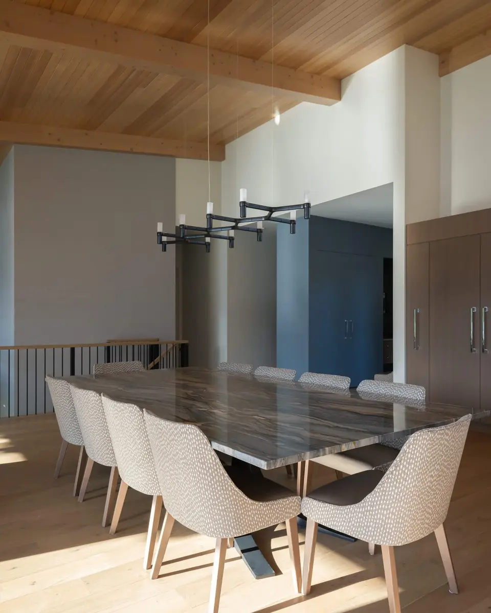 Dining table with a stone slab top and pale chairs, dark millwork wall behind