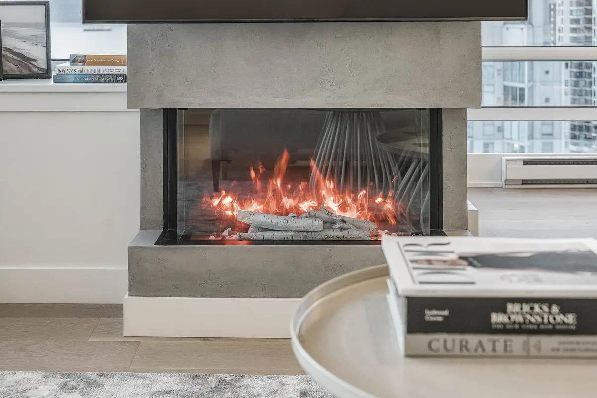 A lit linear fireplace in a grey surround, books on a round table in front