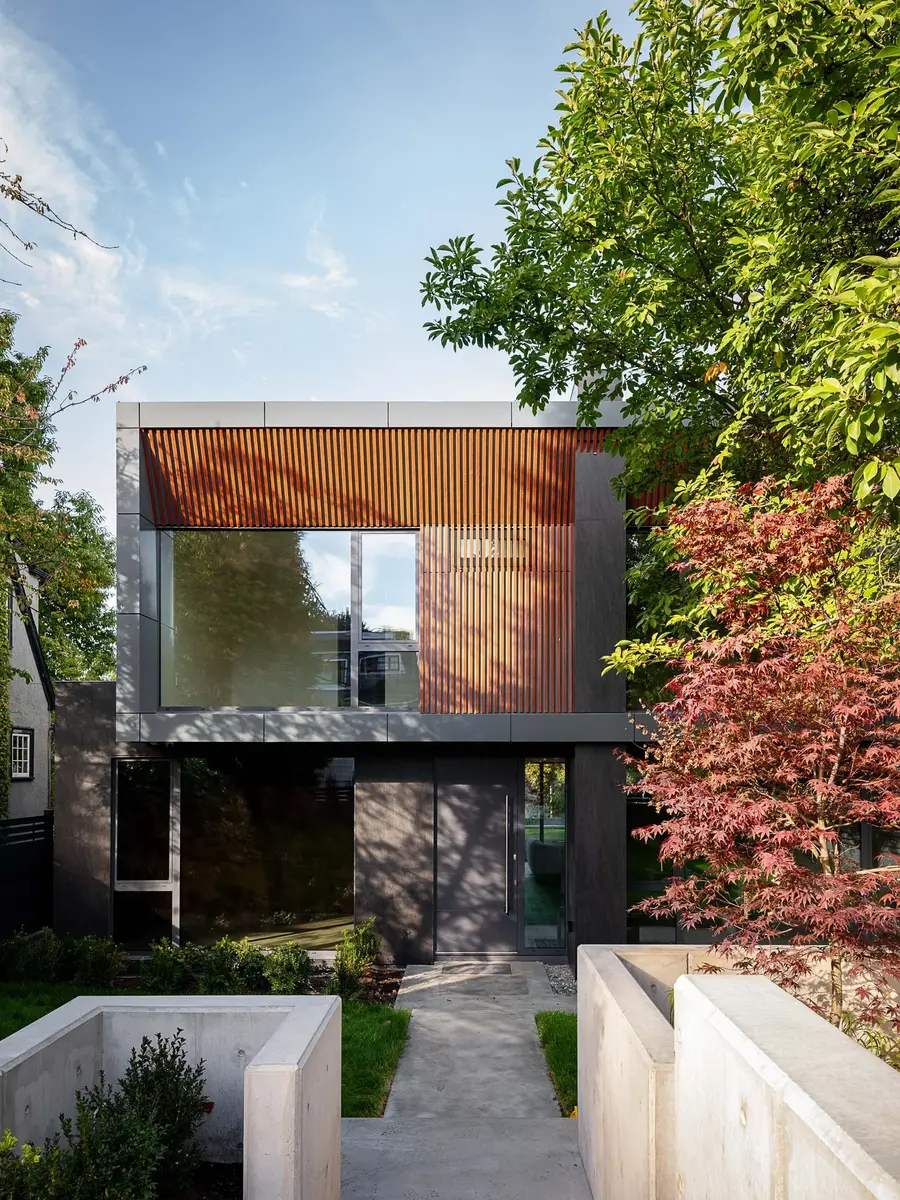 The front elevation seen straight on between trees, a concrete path to the entry