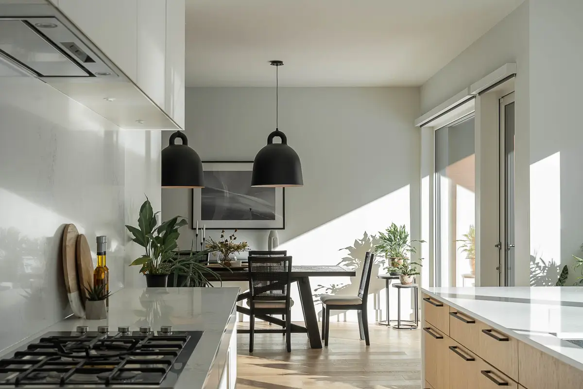 Gas cooktop in a white counter, dining table and dome pendants in the light beyond
