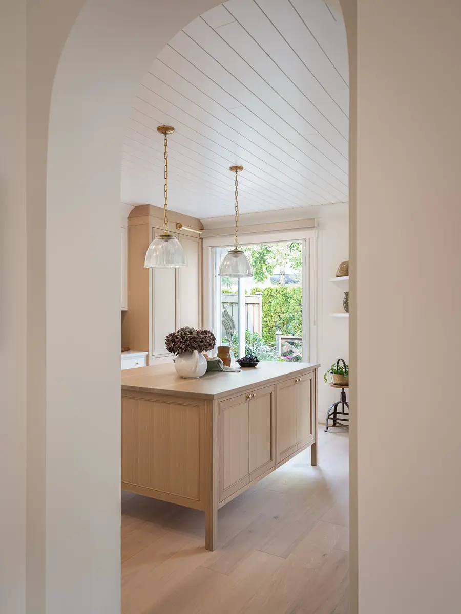 View through an arched opening to the kitchen island and a sliding door onto greenery