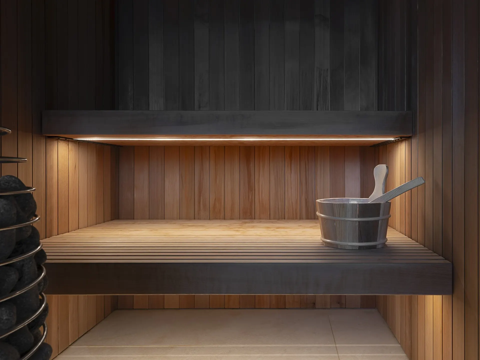 Sauna benches lit from beneath, a wooden bucket and ladle on the upper bench