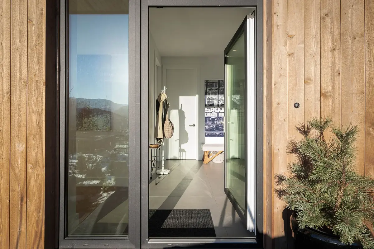 Open entry door in wood siding, looking through to a coat stand and a tiled hall