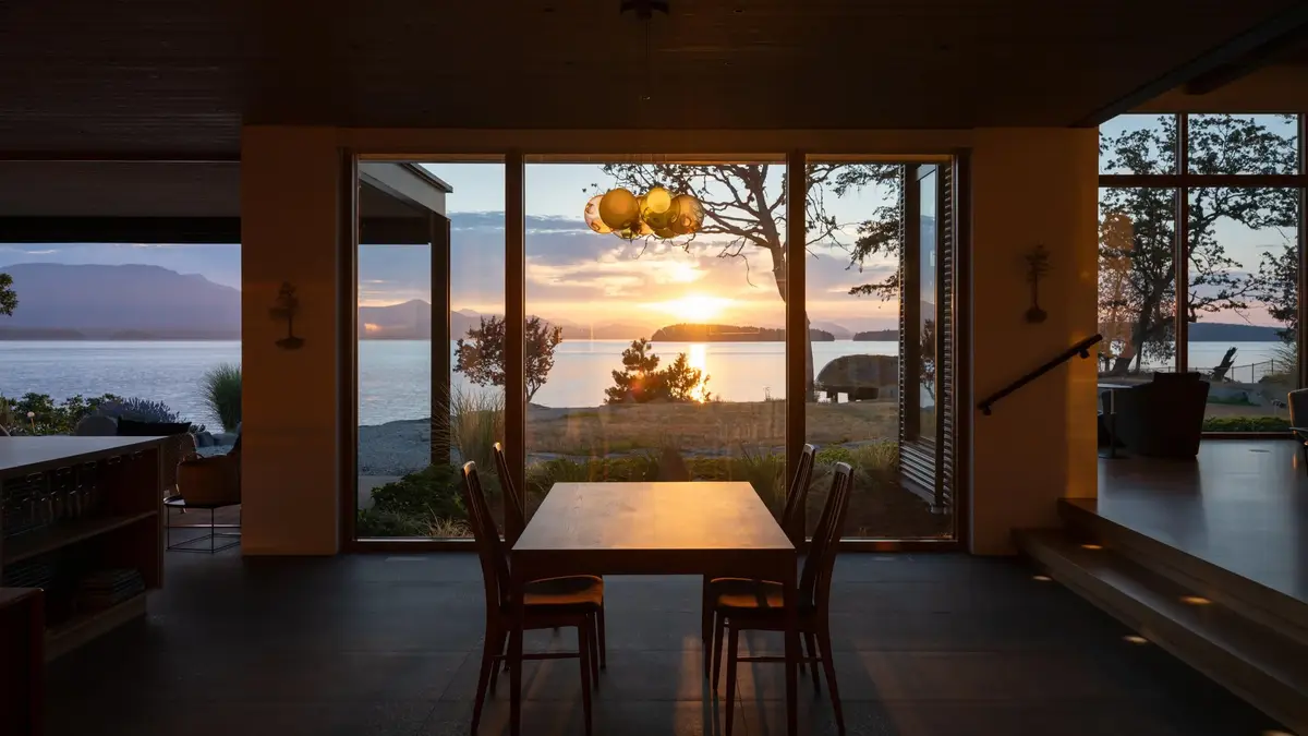 Dining table and glass pendants against open doors and the sun low over the water