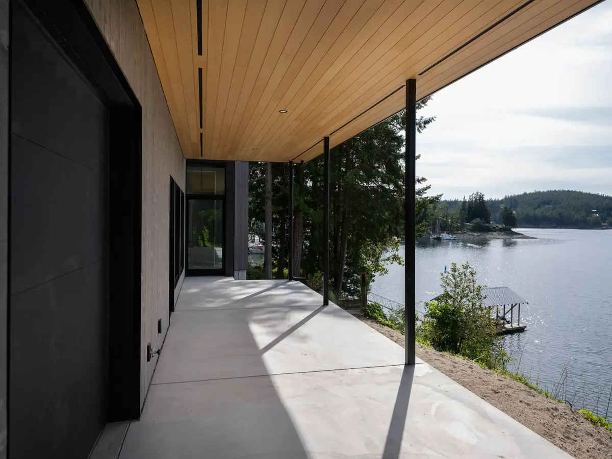 Covered walk on slim dark columns under a pale wood soffit, the bay to the right