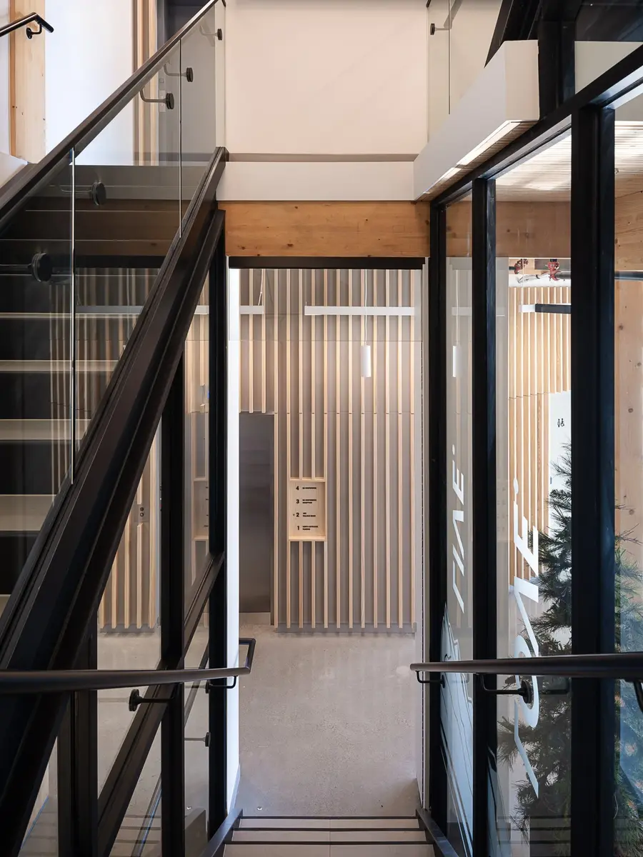 Stair with a black steel rail and glass balustrade, a slatted wood wall alongside