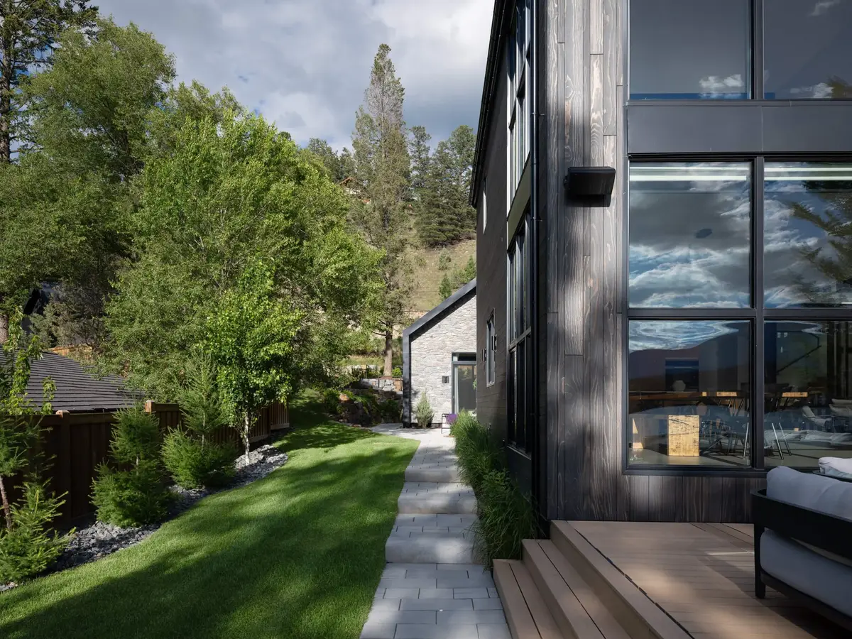 A paved path running between lawn and the dark wood facade, trees along the slope