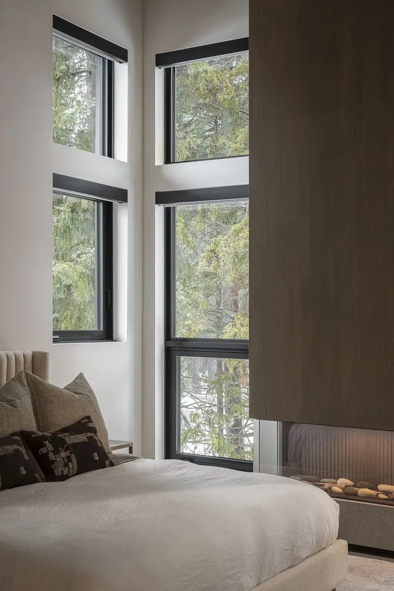 Bed beside a corner of full height glazing, dark panelled wall and trees outside
