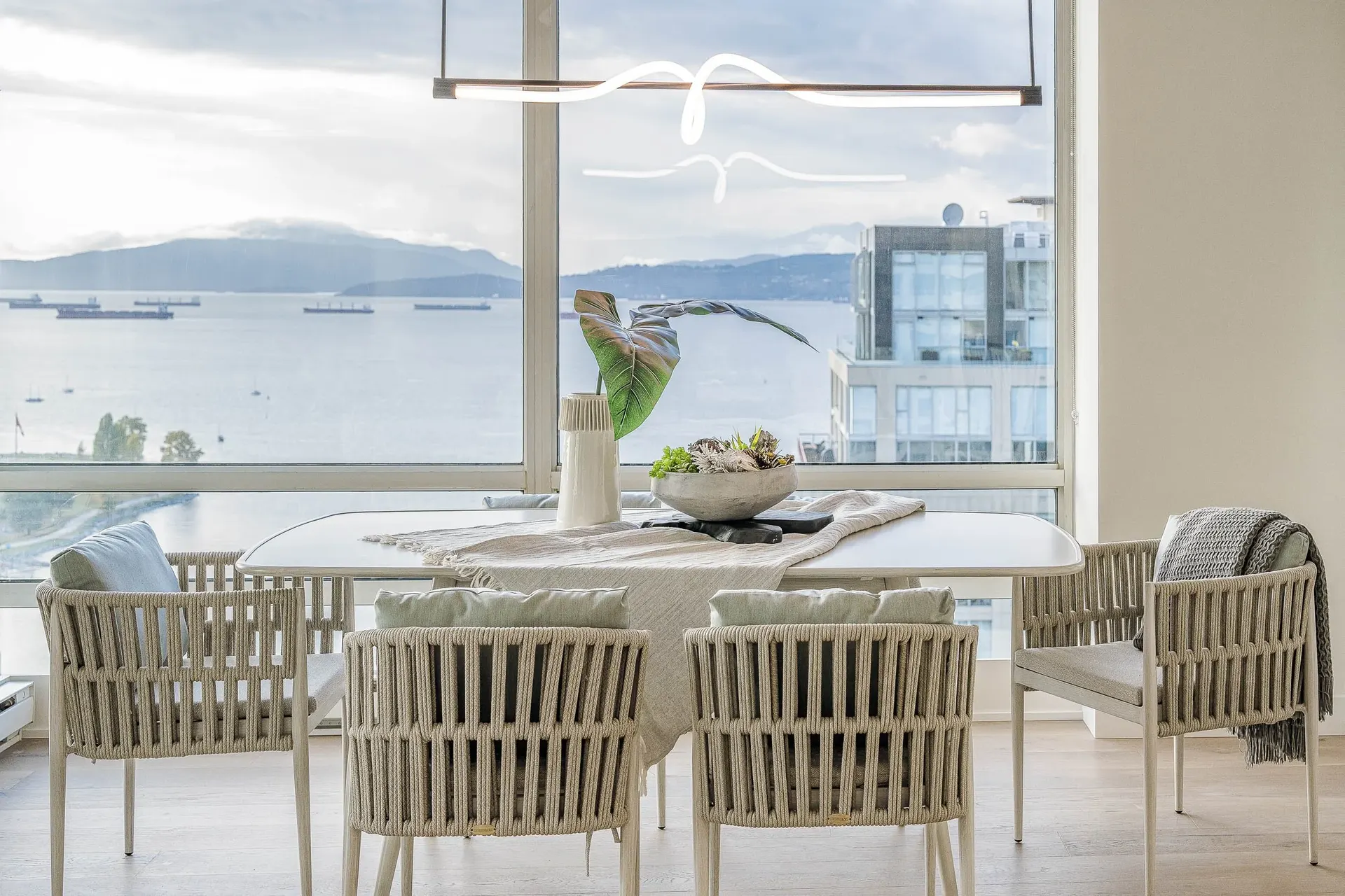 Dining table and woven chairs at the glass, ships at anchor and mountains across the water