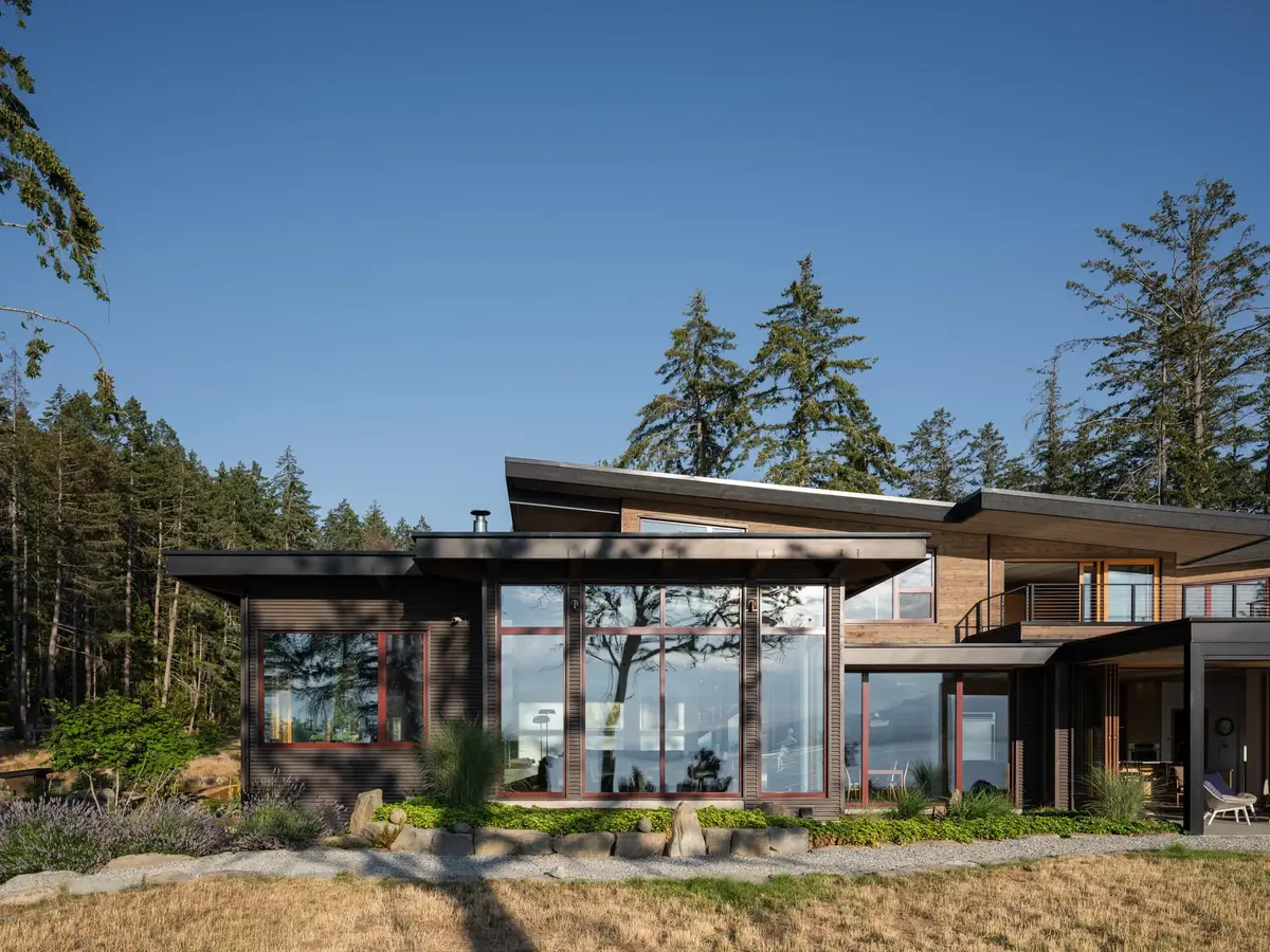 The house across dry grass, red framed glazing under a long low roof