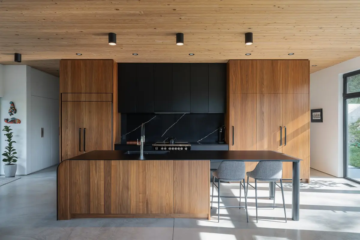 Kitchen with wood fronted cabinetry either side of a black cooking wall, island and stools in front