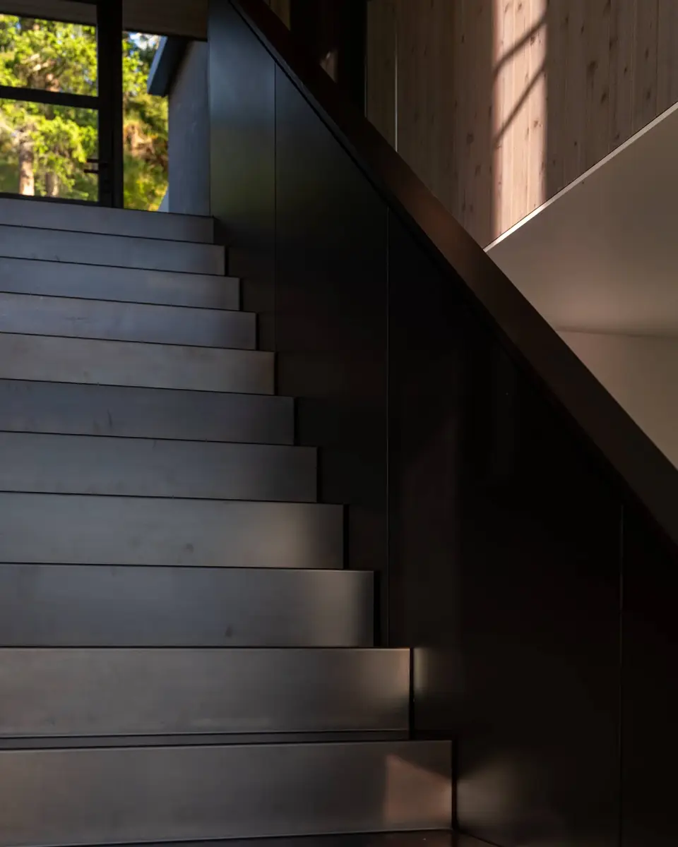 Dark metal stair treads rising toward a window, the guard wall in shadow beside them