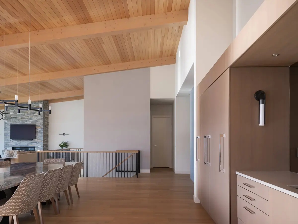 Wood plank ceiling over a hall of tall cabinetry, dining table and stone fireplace beyond