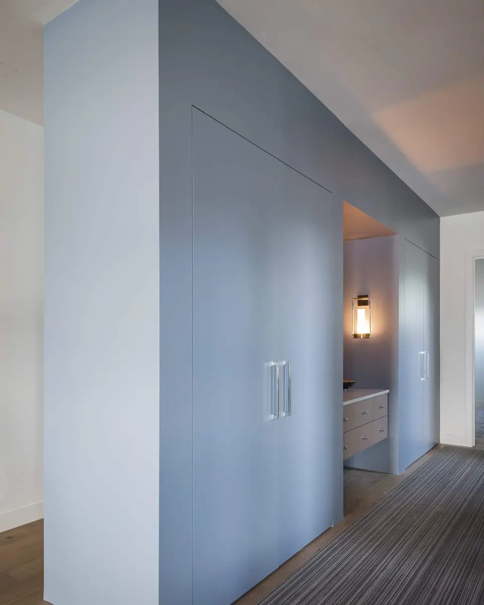 Blue grey millwork turning into a lit alcove with a sconce and a floating vanity