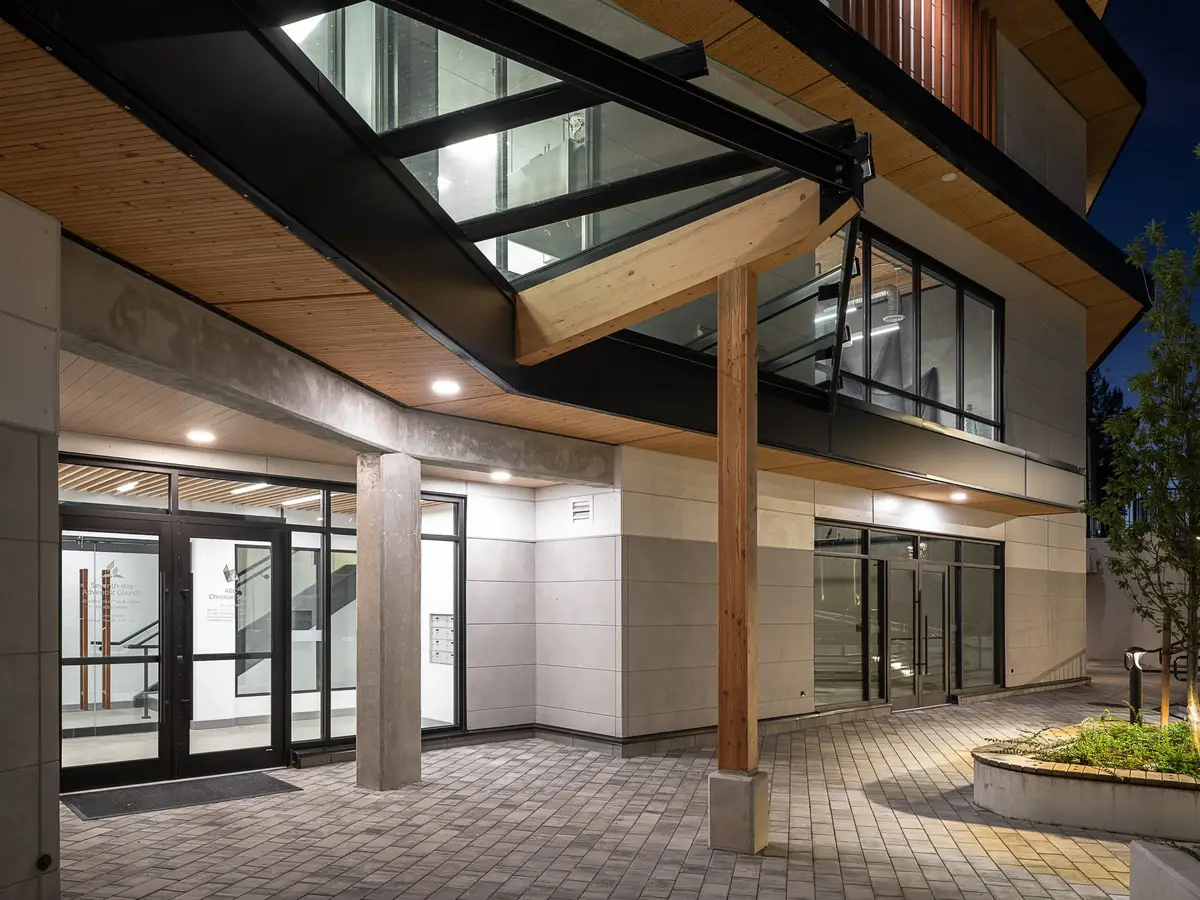 Covered walkway at dusk, downlights in the wood soffit above the entry doors and paving