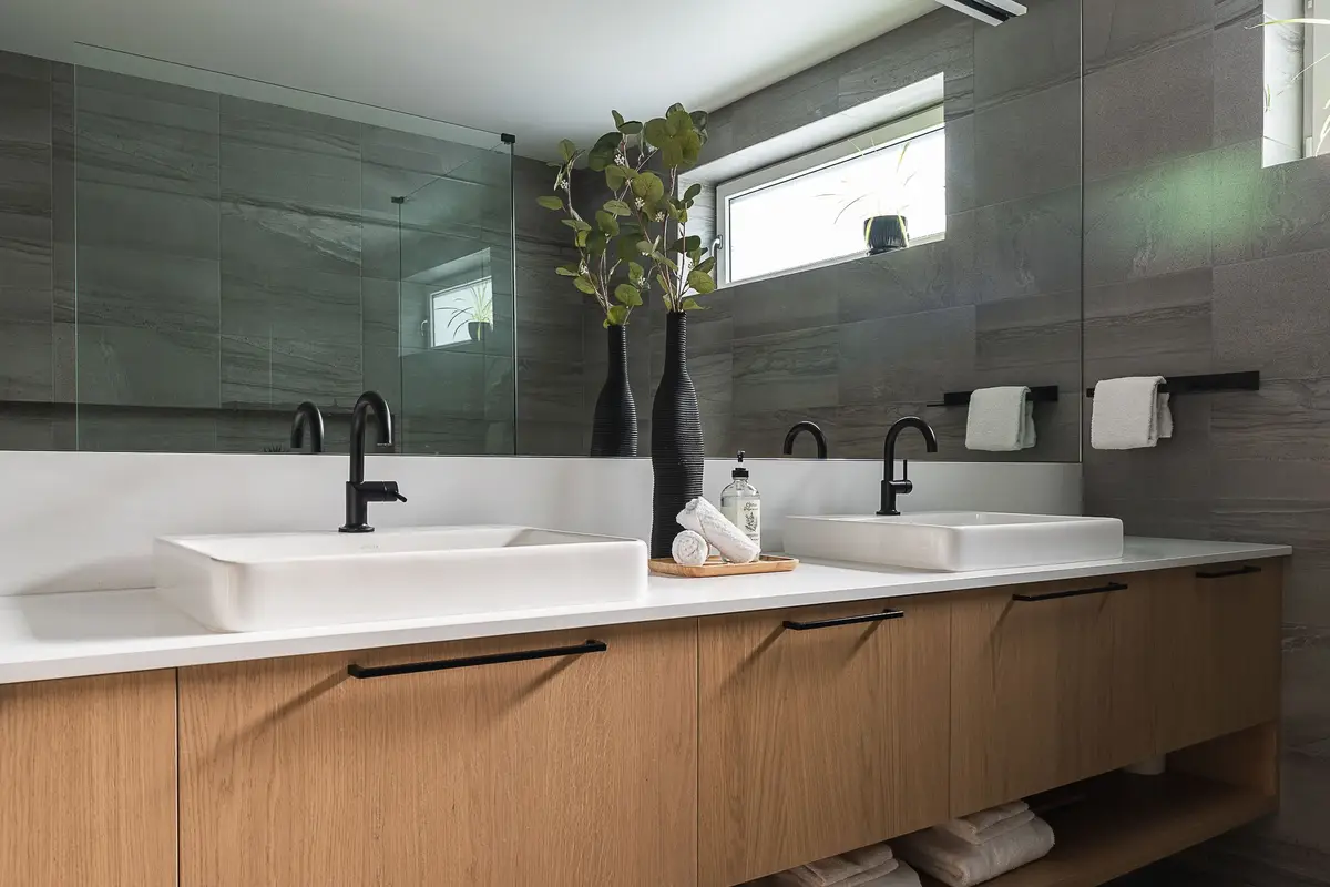 Two white basins on a long vanity, black tapware and grey veined tile behind