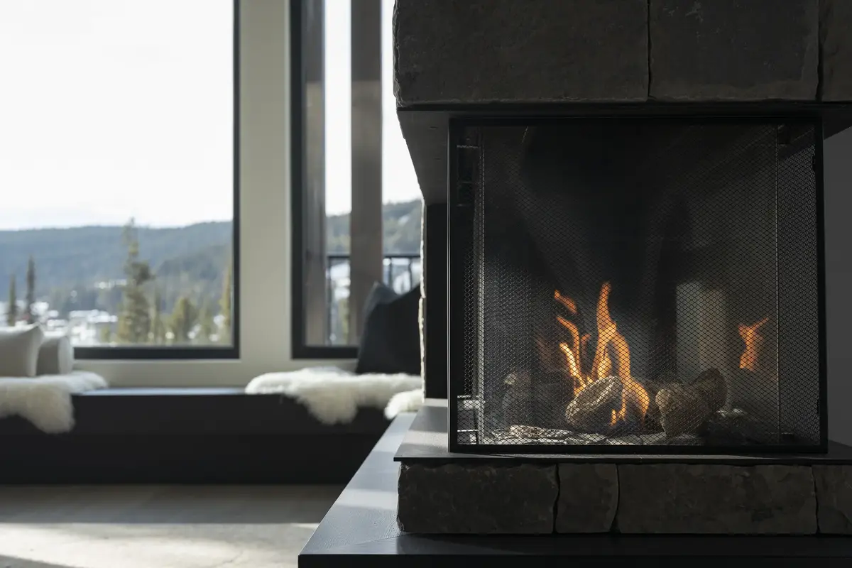 Fire burning in a black firebox beside a window seat, snowy hills beyond