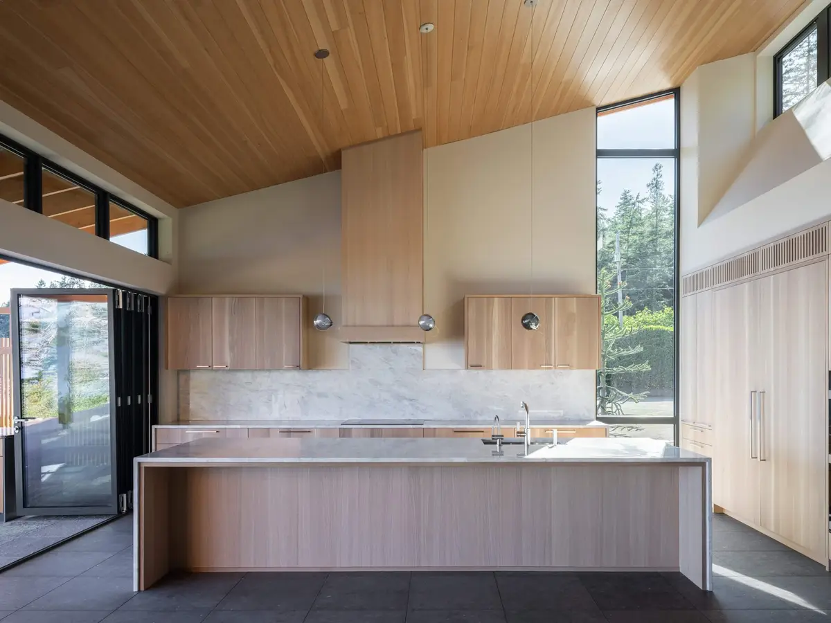Island below a vaulted wood ceiling, tall glazing lighting the end of the room