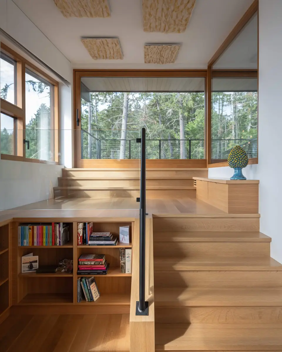 Stair of pale timber with books shelved into its base and a landing above