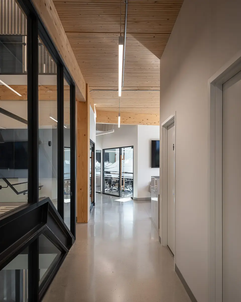 Corridor past a timber column, a screen on the wall and daylight from the glazing
