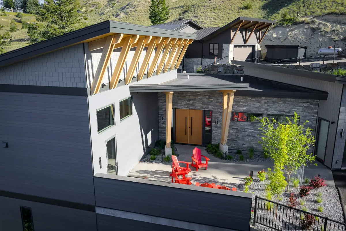 Angled roof of exposed rafters above a stone entry, red chairs on the courtyard paving