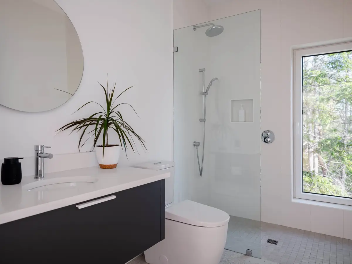 Guest bathroom with a dark floating vanity, round mirror and a walk in shower