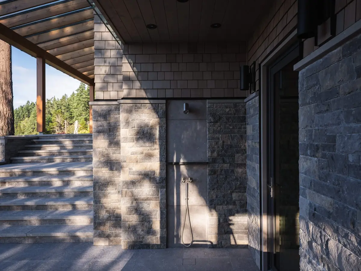 Outdoor shower fixed to a stone wall beside steps rising to the terrace