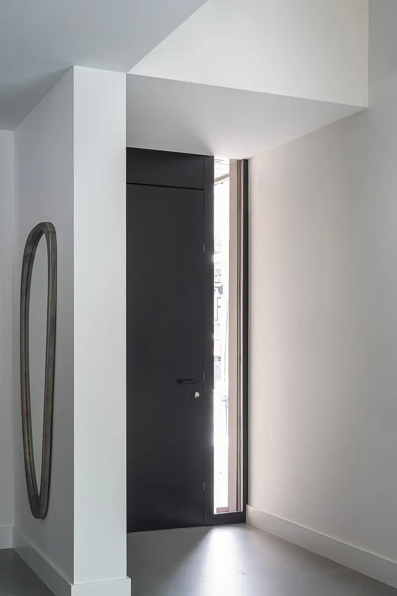 Entry hall with a dark flush door, a tall slot window and an oval mirror
